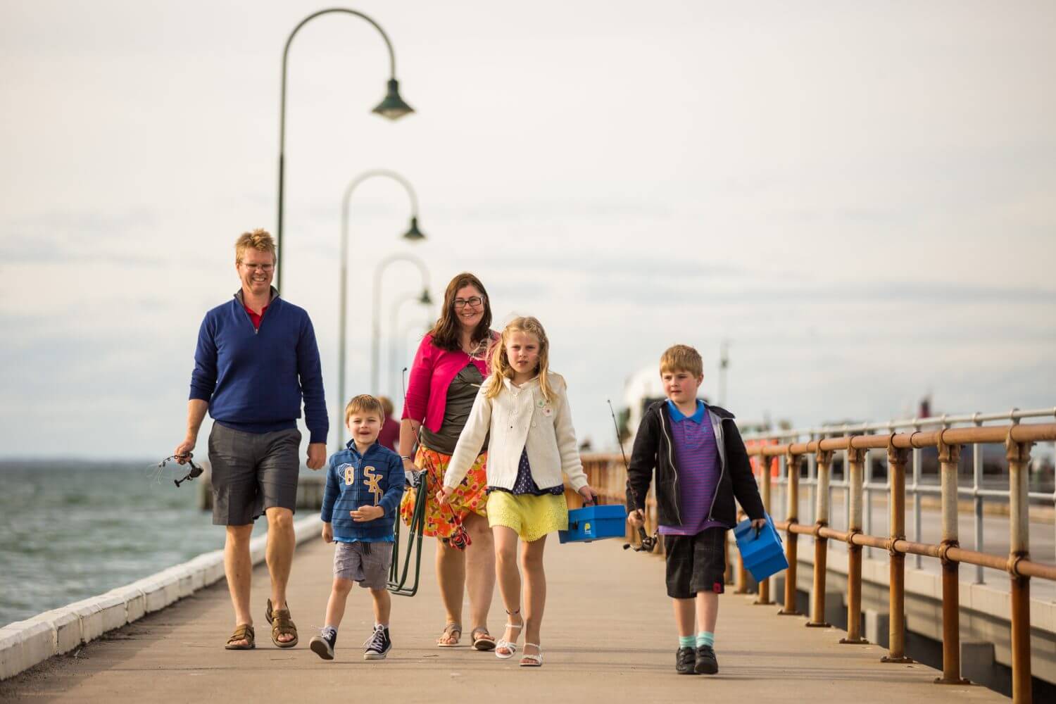 family walking along the boardwalk at the beach with fishing rods